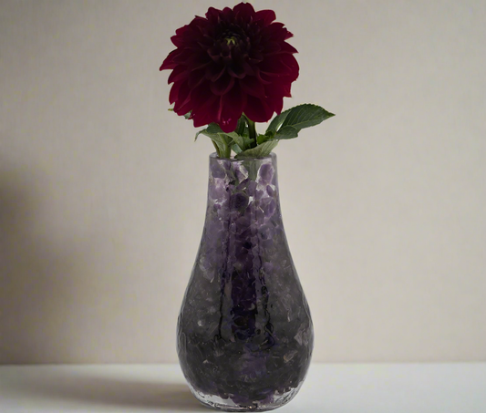 Amethyst crystal vase with a dark red flower against a plain background